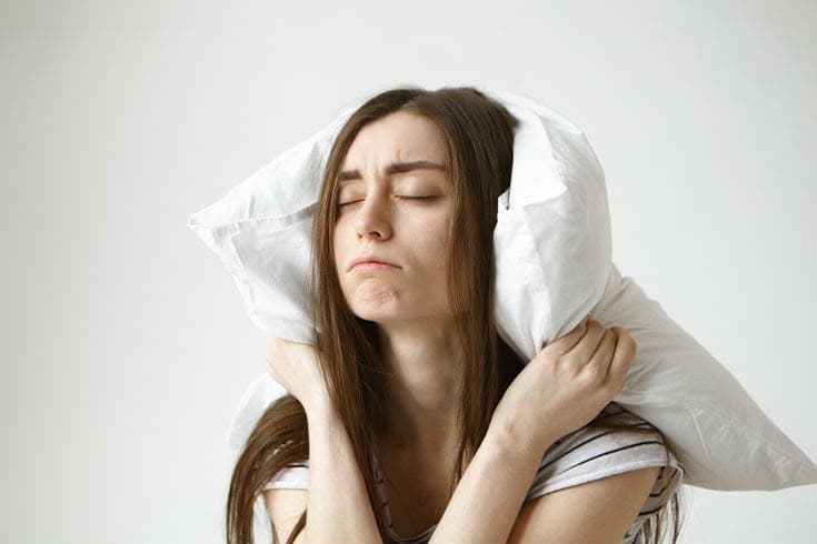 A woman pressing a pillow over her ears, overwhelmed by anxiety